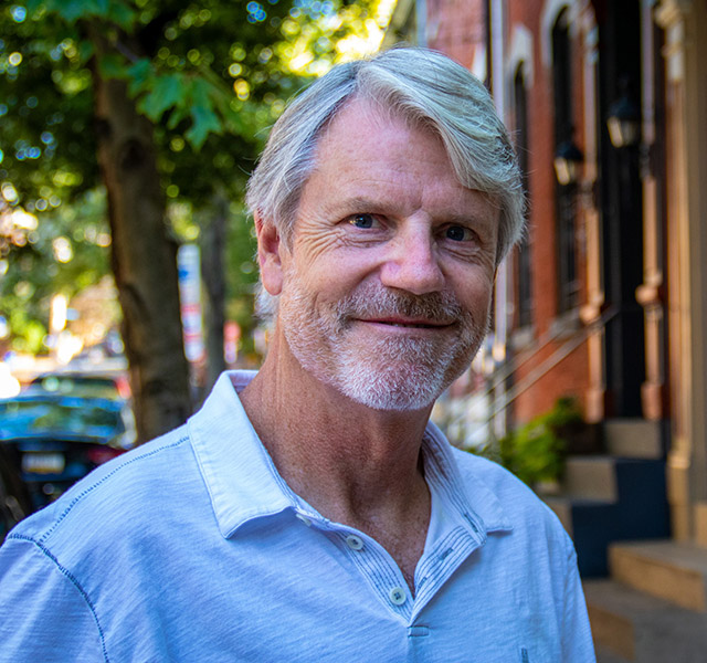 Bearded man in his fifties softly smiles on a charming street in Pittsburgh