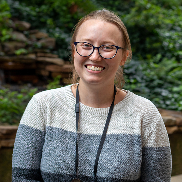 Young woman wearing a name badge lanyard smiles outside.