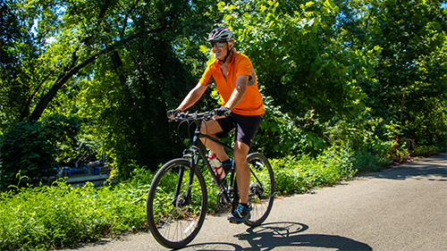 Benefits_Image Man bikes outside on a lush bike path.