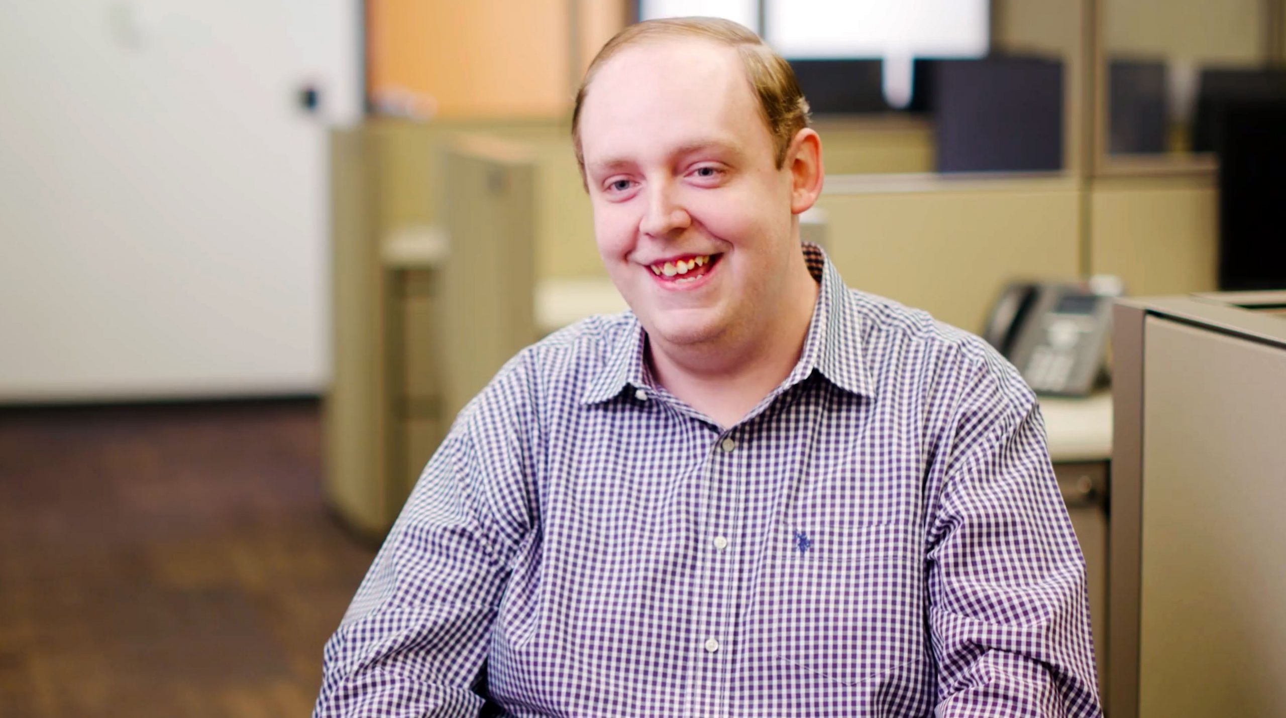 Young man in plaid shirt shirts in office setting.
