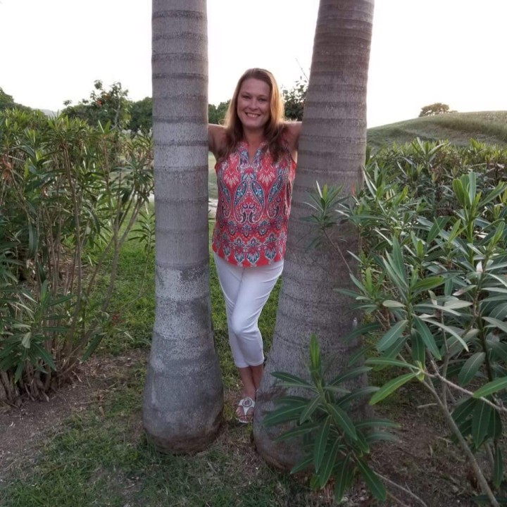Woman stands between two palm trees.