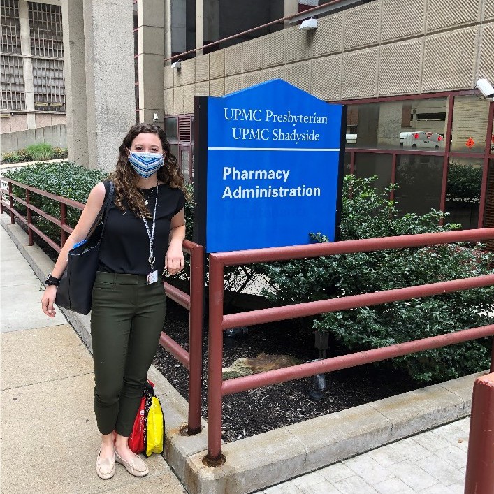 Young woman stands in front of sign outside of hospital.