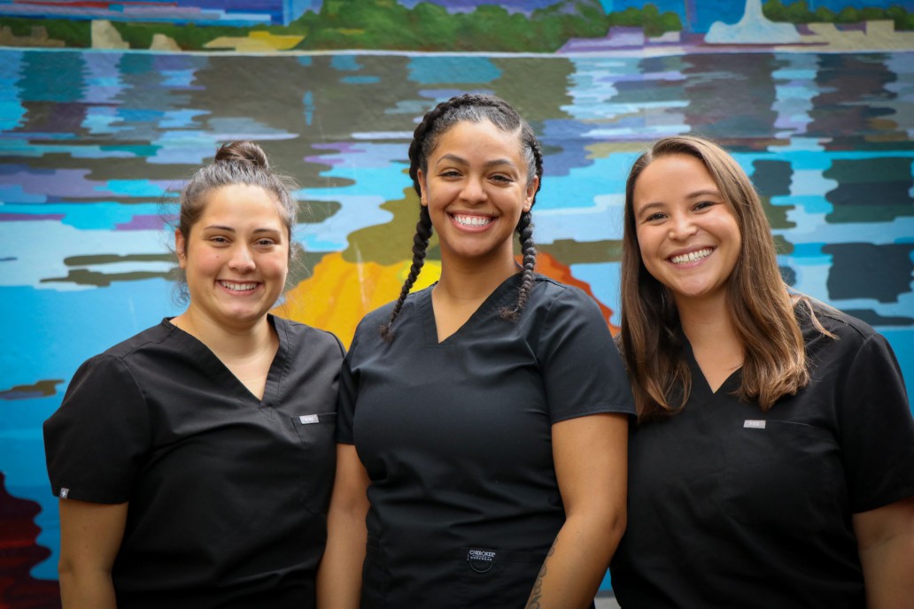 Three behavioral health nurses stand in front of mural, smiling.
