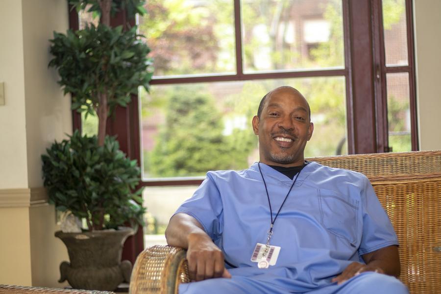 Man sitting on couch in light blue scrubs.