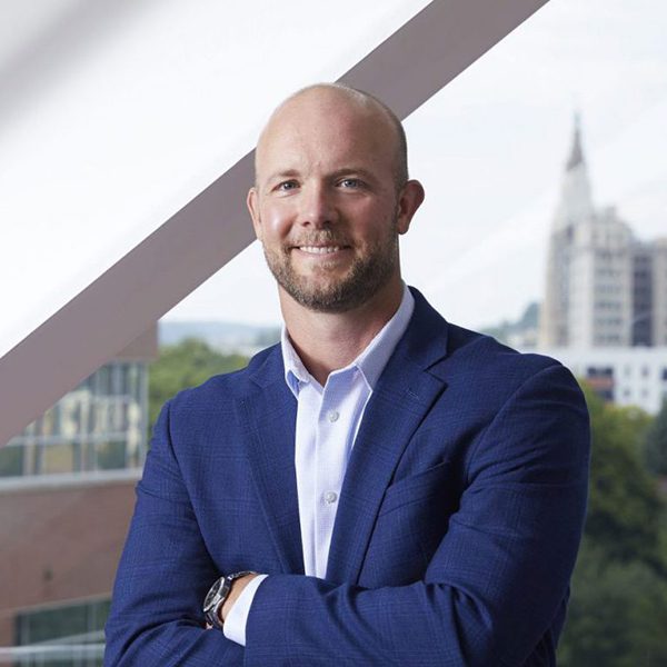 Man in business clothes smiles with cityscape in background.