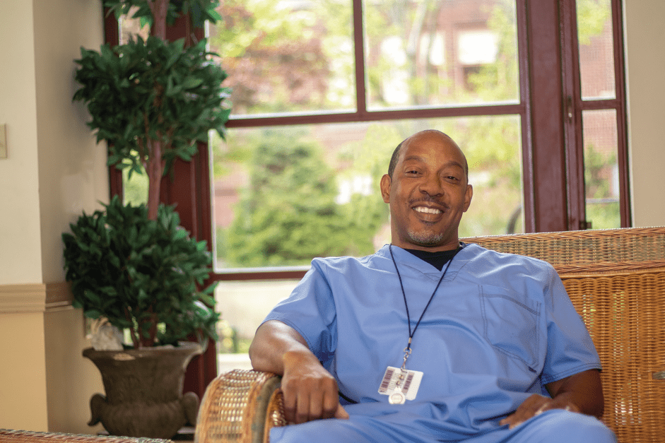 Man in blue scrubs sits in chair.