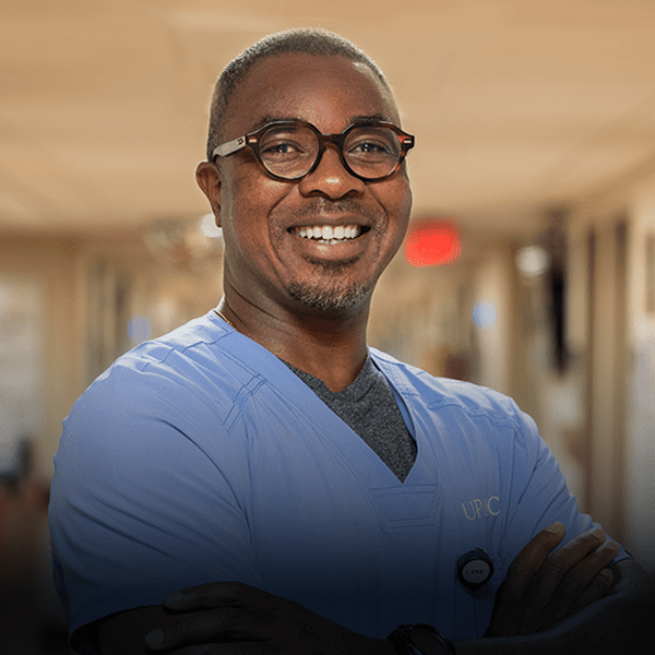 Male nurse wearing glasses stands in hallway.