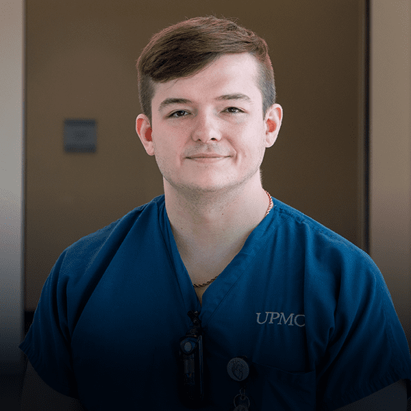 Young man stands in navy scrubs.
