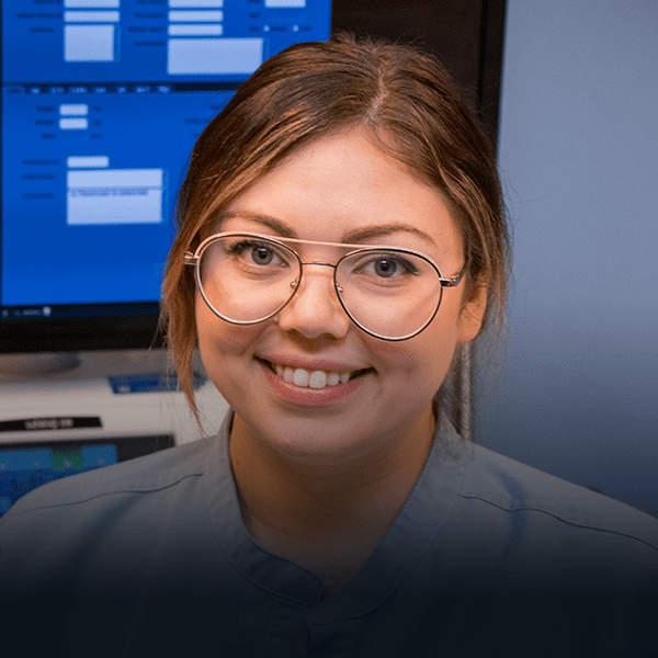 Young woman with glasses stands in hospital near screen.
